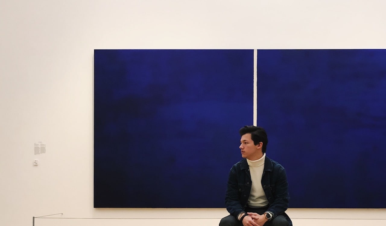 Didier Catz sitting in front of a large blue painting in the Amsterdam Stedelijk Museum.